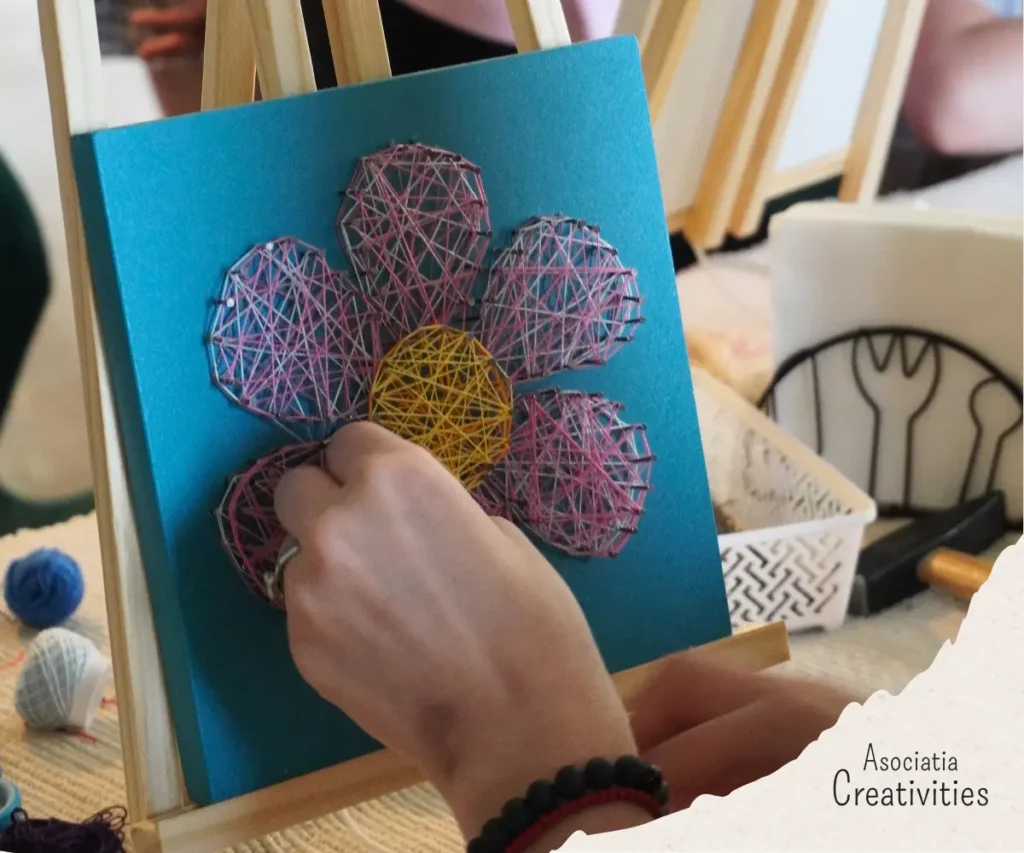 Participant lucrând la un tablou string art cu floare în cadrul atelierului